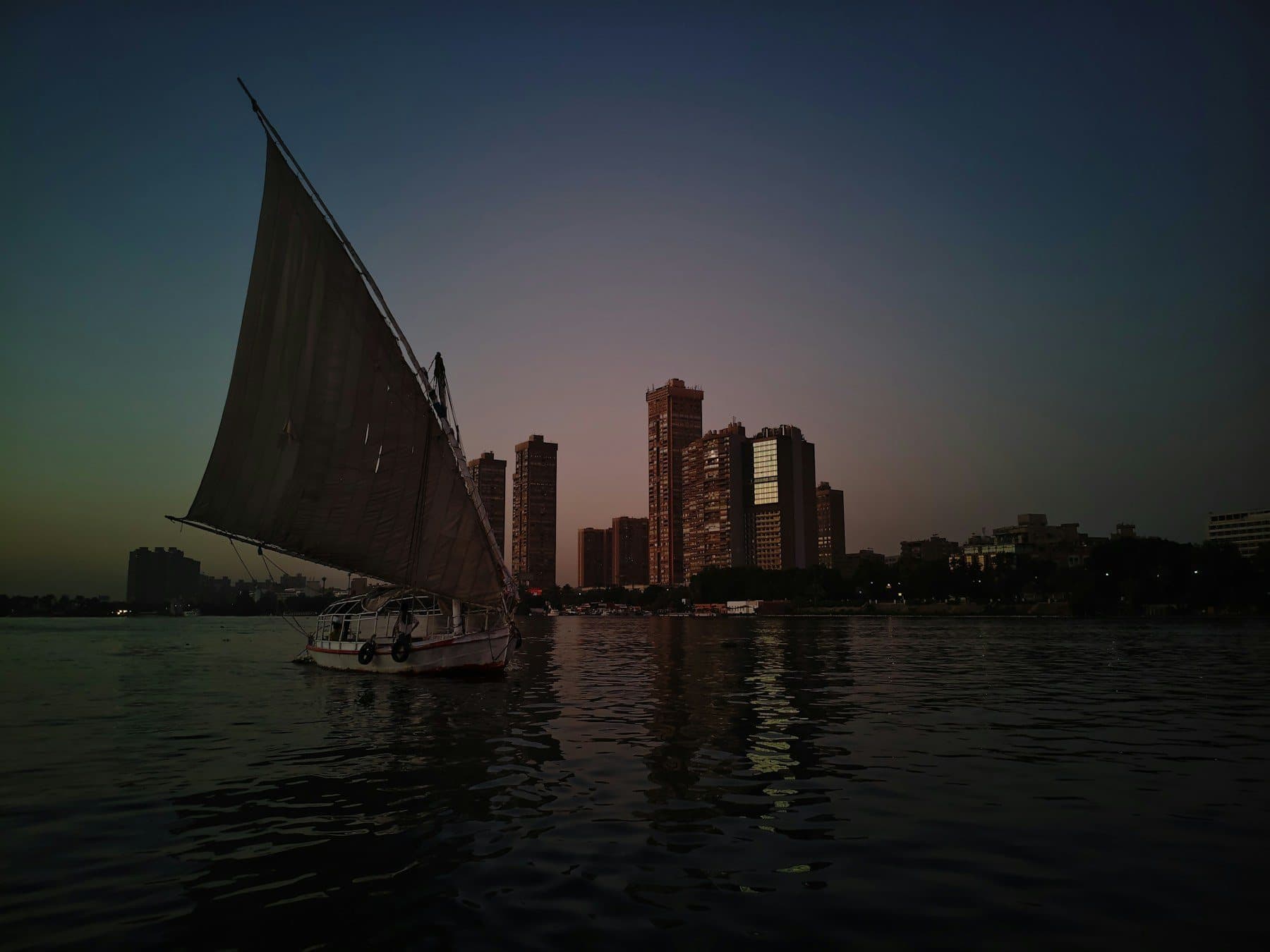 A felucca sailing on the Nile at dusk with the Cairo skyline behind