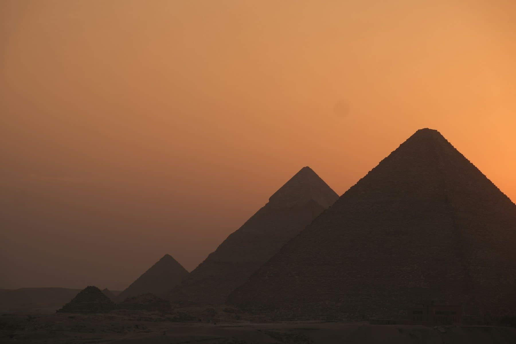 The Pyramids of Giza silhouetted against an amber sunset